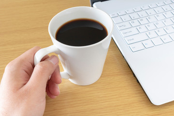 ノートパソコンを操作しながらコーヒーを飲む