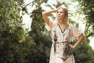 Beautiful blond girl posing at the park in dress