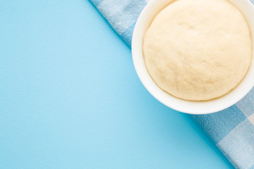 Fresh raw dough in bowl on towel. Ready for baking. Closeup. Empty place for text on light pastel blue table. 