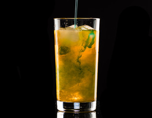 orange cocktail with mint syrup with ice in a glass on a black background