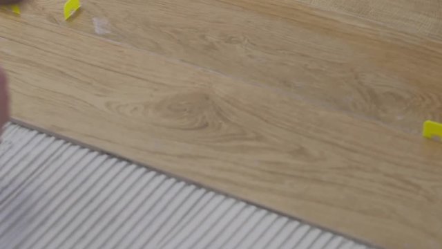 A man places a tile on the floor on top of cement. The tile is of has coloring a cut oak
