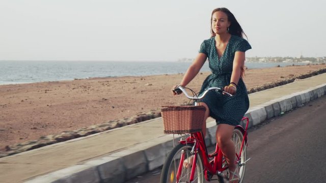 Attractive smiling red hair female ride vintage bicycle along coast line 4k