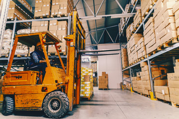 Man driving forklift in warehouse. All around shelves and boxes.