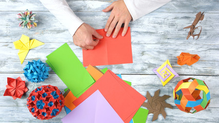 Person folding red paper sheet. Set of origami crafts made by a talented man, top view. Origami exhibition project.