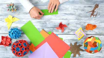 Fototapeta premium Hands making origami with green paper. Person folding green paper sheet. Origami exhibition project.
