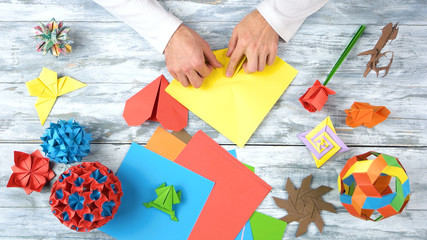 Person folding red paper sheet. Set of origami crafts made by a talented man, top view. Origami exhibition project.