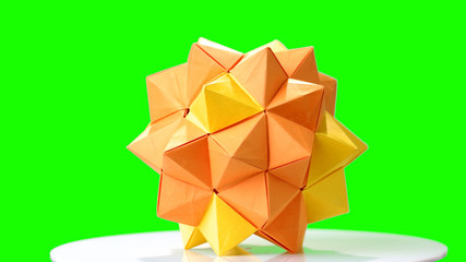 Modular origami flower on green screen. Yellow origami ball on chroma key background. Paper folding and geometry.