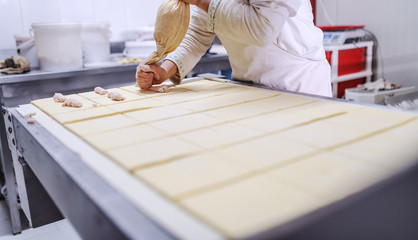 Hardworking baker filling pastry with delicious custard. Bakery interior.