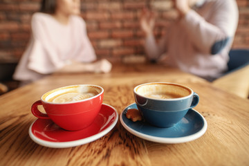 Close up of two cups of fresh espresso. In background couple talking. Cafeteria interior.