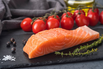 Raw salmon fillet with rosemary and tomatoes on a black stone