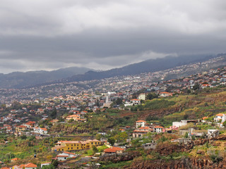 Fototapeta na wymiar a panoramic view of funchal in madeira showing small farms and agriculture with buildings of the city against distant cloudy mountains
