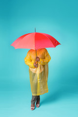 A woman in a yellow raincoat hid under a red umbrella. It stands on a blue background, the face is not visible. Looks like a mushroom.