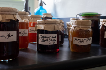A close up of several jars of home made jams sitting on a work top, with old fashioned brown paper and string lids with hand written labels