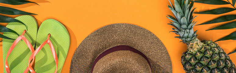 panoramic shot of pineapple, tropical leaves, green flip flops and brown straw hat on orange background © LIGHTFIELD STUDIOS
