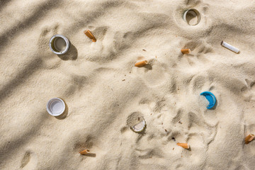 top view of seashells, bottle caps, scattered cigarette butts, plastic bottle caps on sand