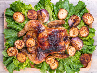 Roasted chicken with grilled potatoes, tomatoes and onion, fresh green salad on wooden table from above. Owen cooked meat with vegetables. Original food serving in restaurant, cafe. Holiday dinner. 