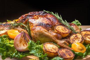 Roasted chicken with grilled potatoes and onion, yellow tomatoes, fresh green salad on wooden table. Owen cooked meat with vegetables. Original food serving in restaurant, cafe. Holiday dinner.