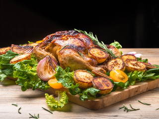 Roasted chicken with grilled potatoes and onion, yellow tomatoes, fresh green salad on wooden table. Owen cooked meat with vegetables. Original food serving in restaurant, cafe. Holiday dinner.