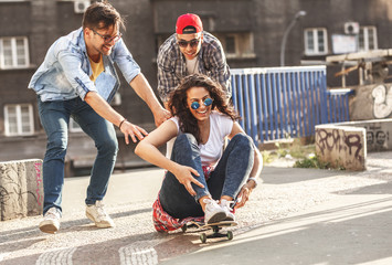 Group of friends hangout at the city street.Female sitting on skate board while friends pushing her from behind.