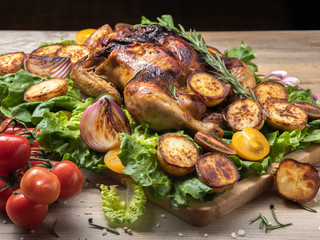 Roasted chicken with red and yellow tomatoes, grilled potatoes and onion pieces, fresh green salad on wooden surface. Owen cooked meat with vegetables. Original food serving. 