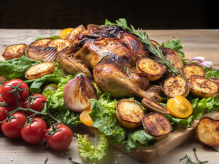 Roasted chicken with red and yellow tomatoes, grilled potatoes and onion pieces, fresh green salad on wooden surface. Owen cooked meat with vegetables. Original food serving. 