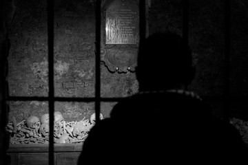 silhouette of a man looking through grate on a pile of skulls and bones in dungeons of Vienna...