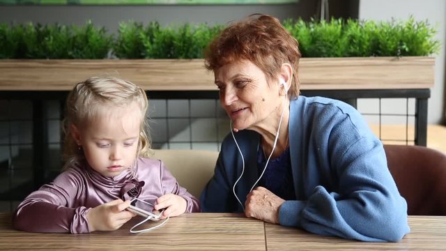 The granddaughter inserted earphones into your grandmother's ears. The little granddaughter turned on the music on the phone and inserted the headphones into her grandmother’s ears.