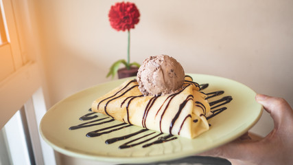 Hand holding cool crepes In the dish topped with chocolate and ice cream.