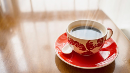 Black coffee is in a red cup with a saucer Placed in the corner on the table have copy space.