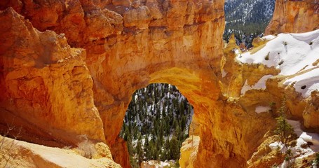 Vertical panning shot of red stone arch and snowy valley in 4K