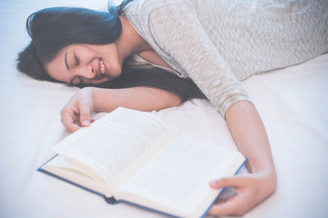 Young woman reading a book on bed at home