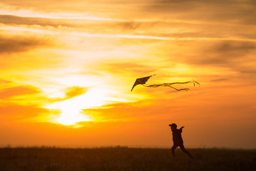 Flying a kite. The boy runs across the field with a kite. Silhouette of a child against the sky. Bright sunset.
