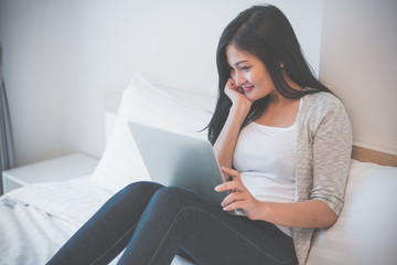Young woman working on a laptop sitting on bed at home