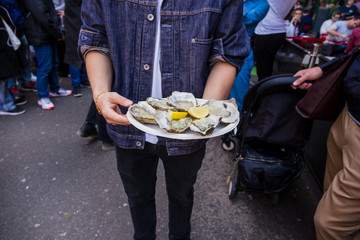Man hand holding fresh raw oyster in paperr plate with lemon in market.