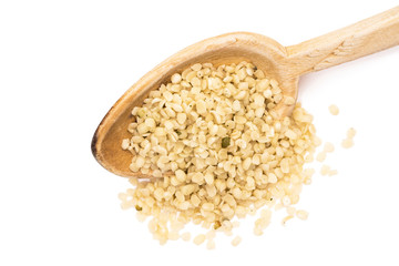 Shelled or peeled hemp seeds on a wooden spoon in a slanted angle seen from above and isolated on white background