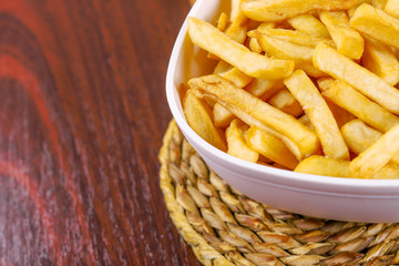 French fries in white bowl on a braided pad on wooden table