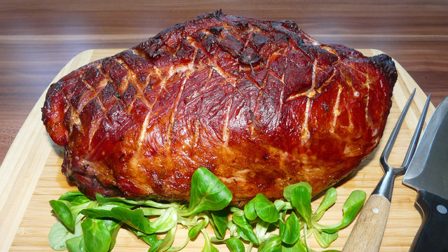 rustikaler Kasslerbraten mit Rautenschnitt angerichtet mit Feldsalat auf einem Bambusholzbrett und Tranchierbesteck