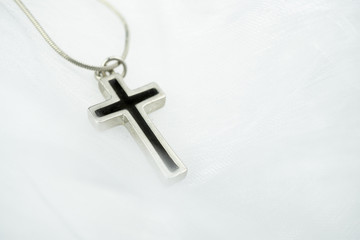 A silver cross with black inlet on a delicate white organza fabric, selected focus