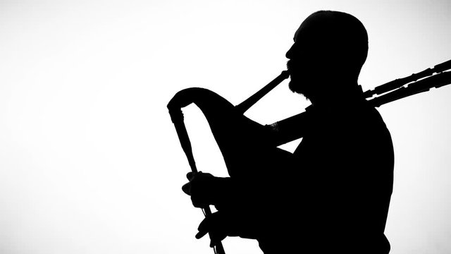 black silhouette on white background man playing bagpipes, national ethnic instrument close up