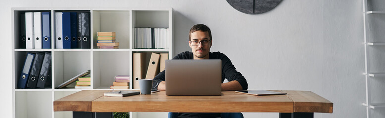 Young man working with computer, phone and tablet at the table while drinking coffee
