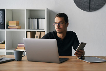 Young man working with phone and computer, receiving phone call, talking with partners 