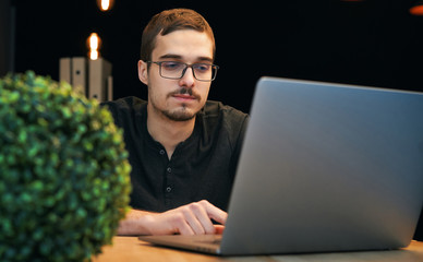 Young man working with computer, phone and tablet at the table while drinking coffee