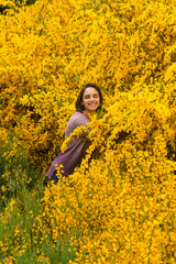 Naklejka na ściany i meble Young, casual, hispanic woman with short hair, smiling, hughing big yellow plant in bloom, in a forest near the mountains in Patagonia, Argentina, full with colorful wild flowers, with copy space