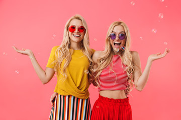 Happy blonde twins in sunglasses having fun with soap bubbles
