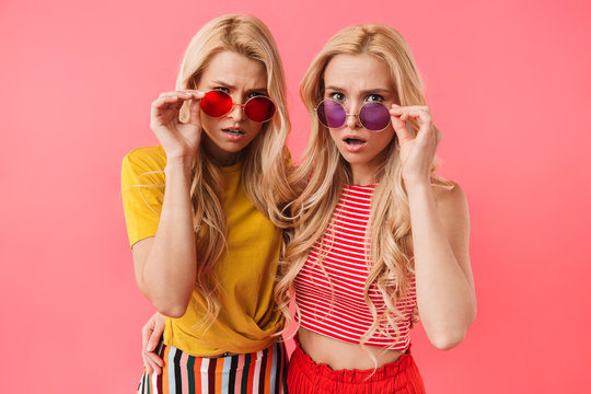 Image of Shocked blonde twins in sunglasses looking at camera