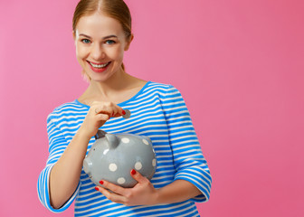 Fototapeta na wymiar happy woman with piggy money bank on pink background. financial planning concept