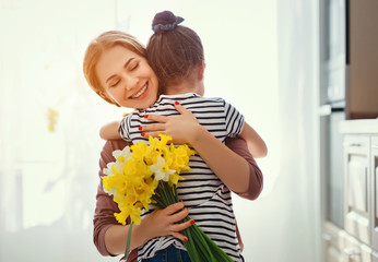 happy mother's day! child daughter   gives mother a bouquet of flowers to narcissus and gift.