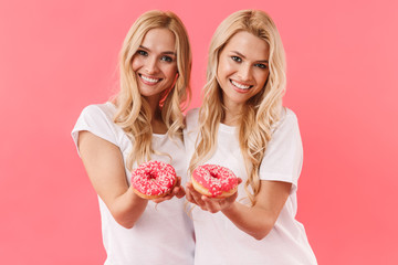 Smiling blonde twins wearing in t-shirts giving donuts