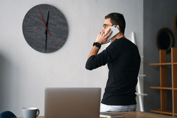 Young man working with phone and computer, receiving phone call, talking with partners 