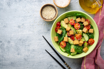 Vegan salad with spinach, cucumber, tomatoes, avocado, fried tofu and sesame. Top view. Copy space.